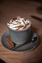 Cup of coffee with cream and cacao powder on it, chocolate next to it, vertical shot