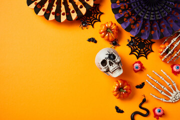 Halloween holiday flat lay composition with paper fans, pumpkins, skull, decorations on orange background. Flat lay, top view.