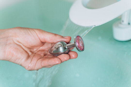 Hands washing metal anal plug, caring for sex toys