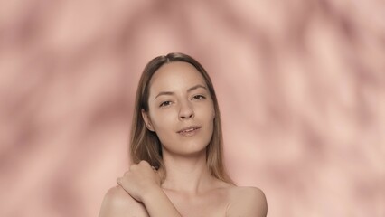 Obraz premium A young woman enjoys her perfect smooth, delicate skin. Portrait of a smiling seminude woman, isolated on a pink background close up. The concept of beauty, cosmetology, skin care, spa.