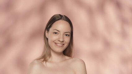 Obraz premium Portrait of a smiling seminude woman on a pink background close up. A woman with natural makeup looks straight ahead. Beauty concept. Natural beauty, cosmetology, skin care.