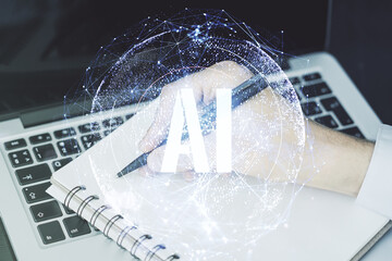 Creative artificial Intelligence symbol concept with hand writing in diary on background with laptop. Double exposure