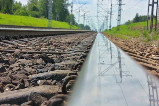 Beautiful smooth rail with a mirror surface of the railway bed reflecting the track posts and the gray sky 