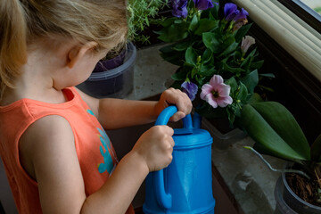 Cute little girl watering a houseplant in a pot at home