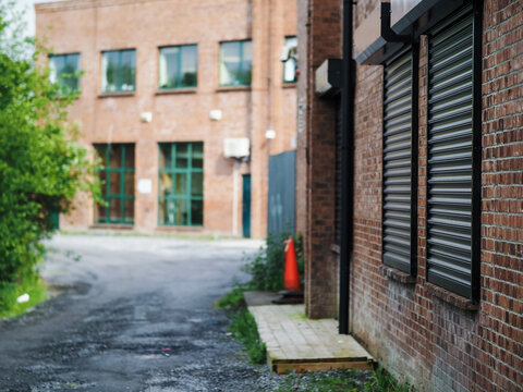 Small path in a back of an office building with security metal shutters over windows. Selective focus. Protection from brake in. Working in a dangerous city area concept.