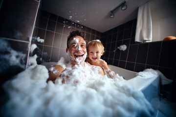 Father and young boy sharing a playful and joyous moment in a lot of bath foam - obrazy, fototapety, plakaty