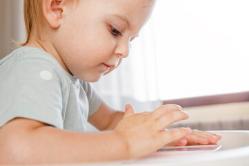 Little child plays with mobile smart phone sitting on highchair