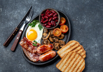 Full fry up English breakfast with fried eggs, sausages, bacon, black pudding, beans, toast and coffee, dark background