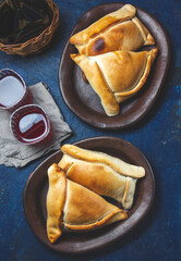 Tipical Chilean baked empanadas de pino y napolitano on clay plates with wine. Dish and drink on 18 September party Independence day Chile, blue background.