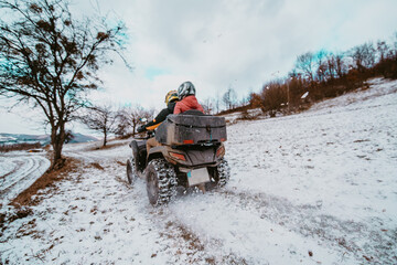 Obraz premium A young adventurous couple embraces the joy of love and thrill as they ride an ATV Quad through the snowy mountainous terrain