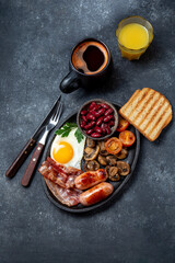 Full fry up English breakfast with fried eggs, sausages, bacon, black pudding, beans, toast and coffee, dark background