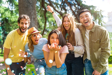 Multiethnic group of partying throwing confetti smiling in the park, fun with friends concept