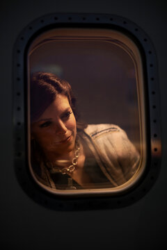Middle aged woman sitting in cabin of private plane looking out of window admiring the sunset, view from outside of plane 