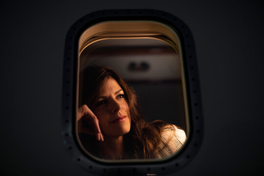 Low angle close up portrait of Middle aged woman sitting n cabin of private plane looking out of window with contemplative look, view from outside of plane 