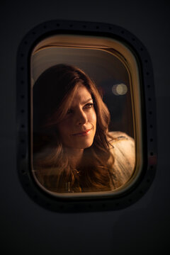 Middle aged woman sitting in cabin of private plane looking out of window viewing the sunset, view from outside of plane 