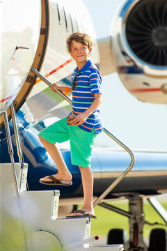 Young boy using stairs to board private jet looking towards camera while holding a seashell 