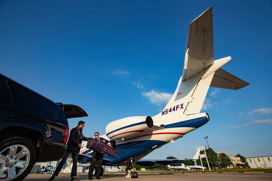 Pilot helping man with luggage from SUV preparing to board Jet on tarmac of small airport
