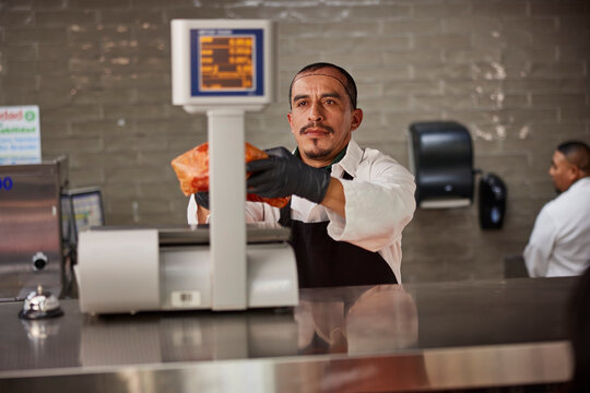 Butcher weighing selection for customer at counter of meat market in grocery store