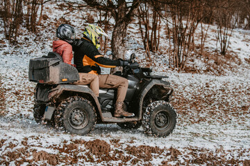 Fototapeta na wymiar A young adventurous couple embraces the joy of love and thrill as they ride an ATV Quad through the snowy mountainous terrain