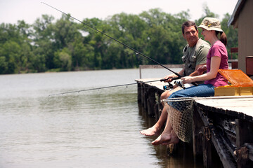 Mature couple sitting on dock fishing on small lake 