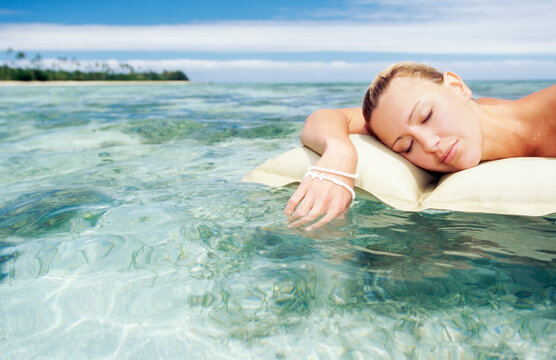  Young woman resting on lilo in tropical water and island in background