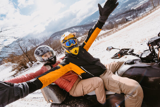 A young adventurous couple embraces the joy of love and thrill as they ride an ATV Quad through the snowy mountainous terrain