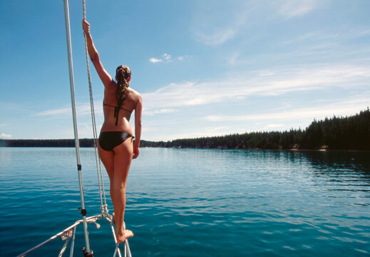  Young woman standing on bow railing of boat in calm water 