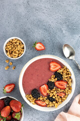 Smoothie bowl with strawberries, blackberries and granola on a blue background. Healthy breakfast. Top view. Copy Space.