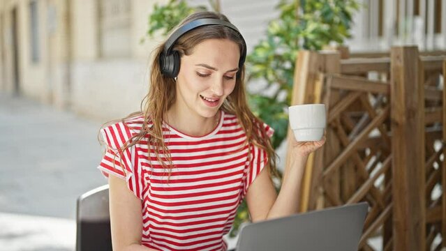 Young blonde woman listening to music and dancing drinking coffee at coffee shop terrace