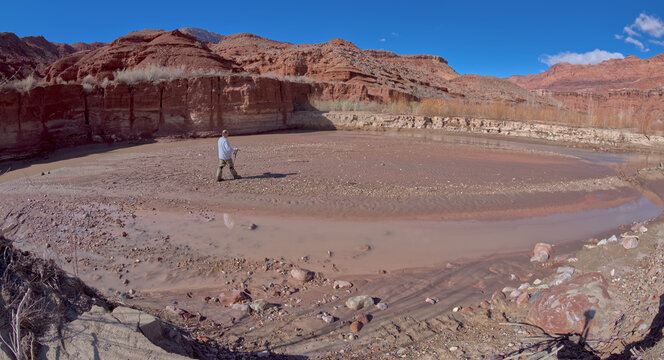 A hiker walking onto a sandbar in the Paria River flowing through Paria Canyon in the Glen Canyon Recreation Area Arizona.
