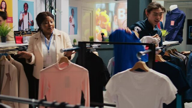 Shoppers hunting for bargains in outlet, buying clothes on impulse during black friday promotional sales. Clients looking through clothing items on hangers while shopping in clothing store.