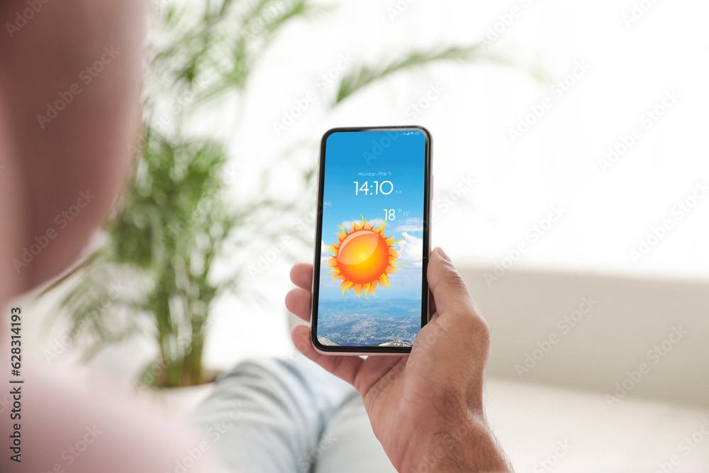 Wall mural man checking weather using app on smartphone at home, closeup. data and illustration of sun on scree