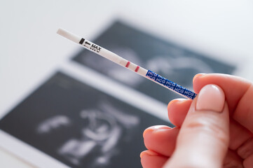 Woman holding a positive pregnancy test on the background of a photo with an ultrasound. 