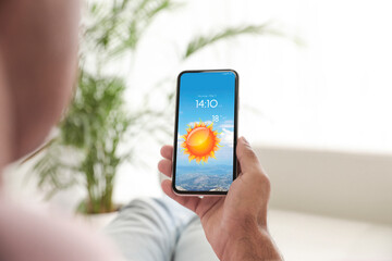 Man checking weather using app on smartphone at home, closeup. Data and illustration of sun on screen