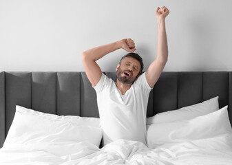 Sleepy man stretching in soft bed at home in morning