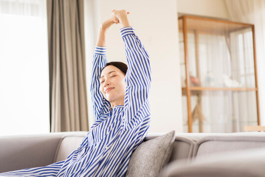 リビングでソファーに座りくつろぐ日本人ミドル女性/ストレッチ