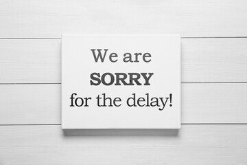 Canvas with phrase We Are Sorry For The Delay on white wooden background