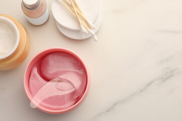 Jar of under eye patches with spoon and cosmetic products on white marble table, flat lay. Space for text