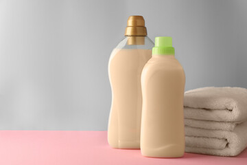 Bottles of fabric softener and stacked clean towels on pink table against light grey background, space for text