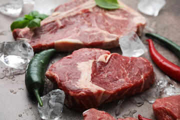 Fresh raw cut beef, ice cubes and spices on brown table, closeup
