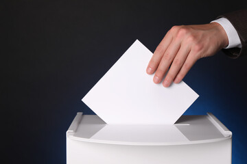 Man putting his vote into ballot box on dark blue background, closeup. Space for text