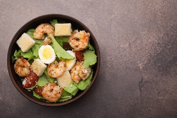 Delicious Caesar salad with shrimps on brown table, top view. Space for text