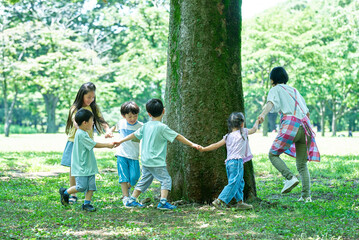 手を繋いで、木の周りを回る子供たちと女性