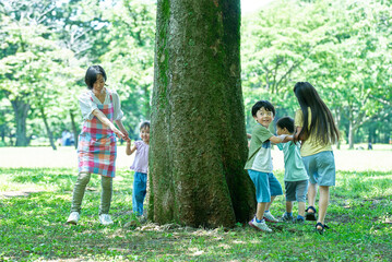 Fototapeta premium 手を繋いで、木の周りを回る子供たちと女性