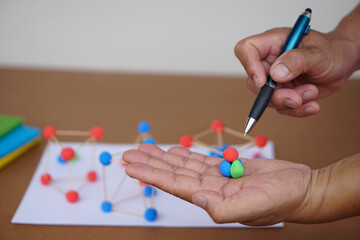 Close up teacher hands hold pen and scientific model teaching aid to teach about molecular structures, made from plasticine balls . Concept, science education. Describing and analyzing.  