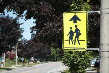 close on neon yellow school zone sign in black with up arrow next to long residential street