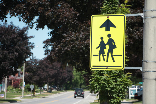 close on neon yellow school zone sign in black with up arrow next to long residential street with vehicle driving away in background