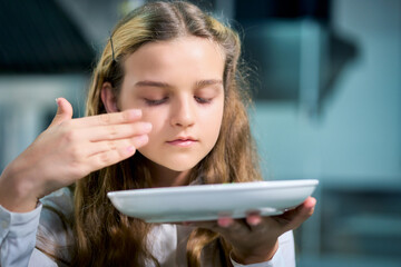 Closeup ro face of signle young girl chef to learn to smell of food for testing method in kitchen.