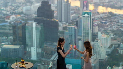 Asian woman friends celebrating dinner party together at skyscraper rooftop restaurant bar in the...