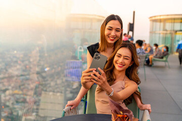 Asian woman friends enjoy urban lifestyle using mobile phone taking selfie together during have...